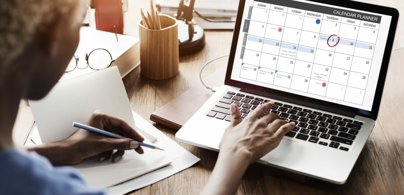 Someone reviews a calendar on their laptop while making notes with a pencil