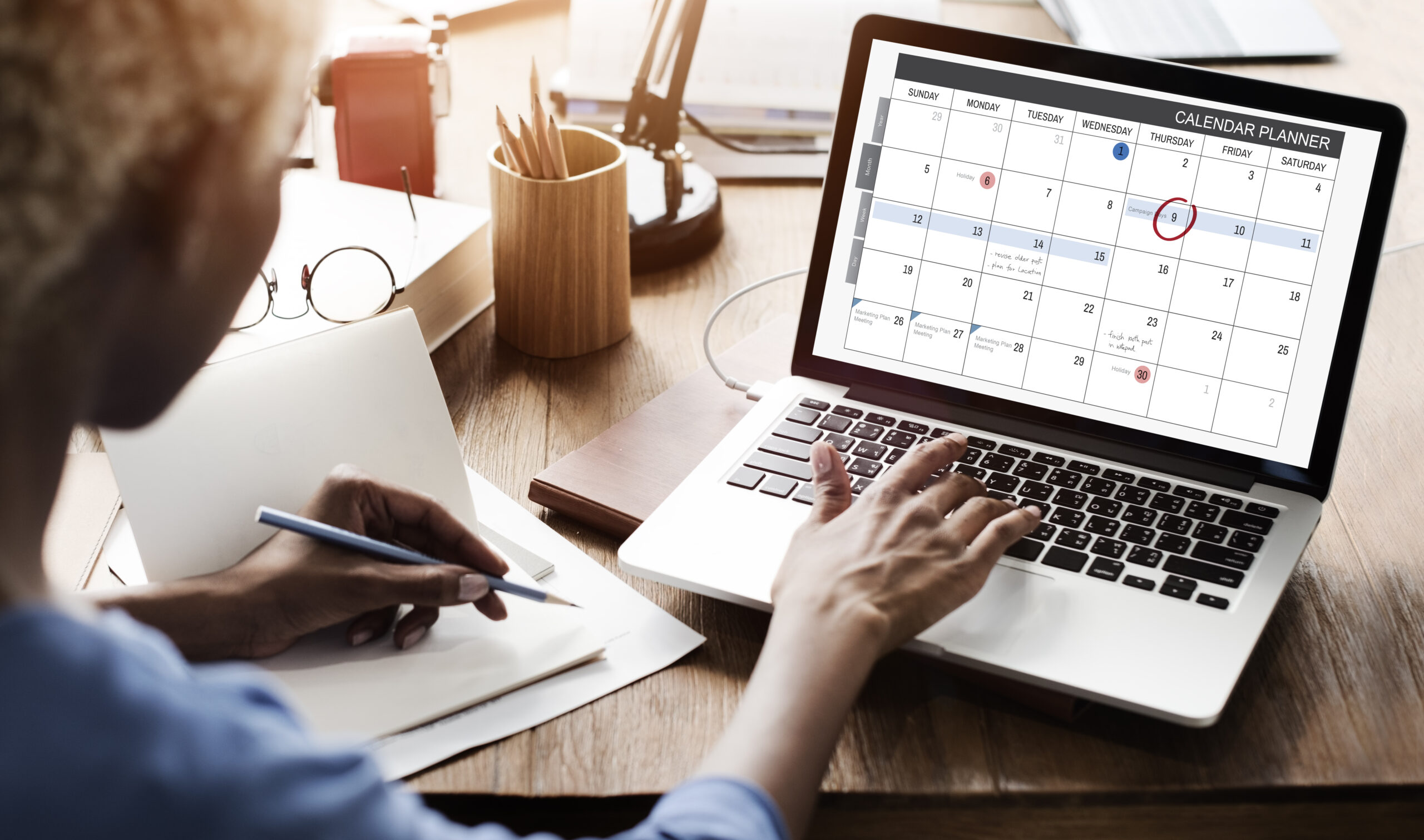 Someone reviews a calendar on their laptop while making notes with a pencil