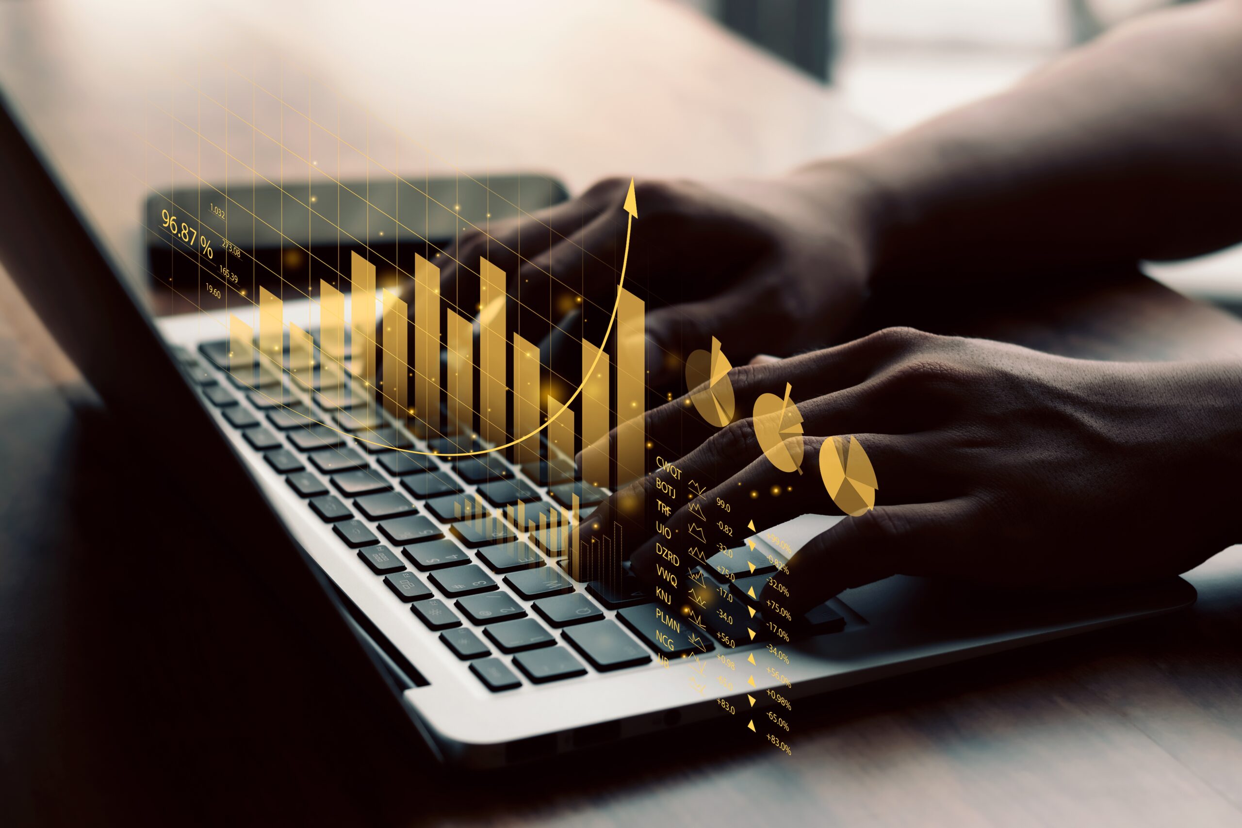 Someone sits at a table typing on a laptop. Images of graphs and charts are imposed over the keyboard