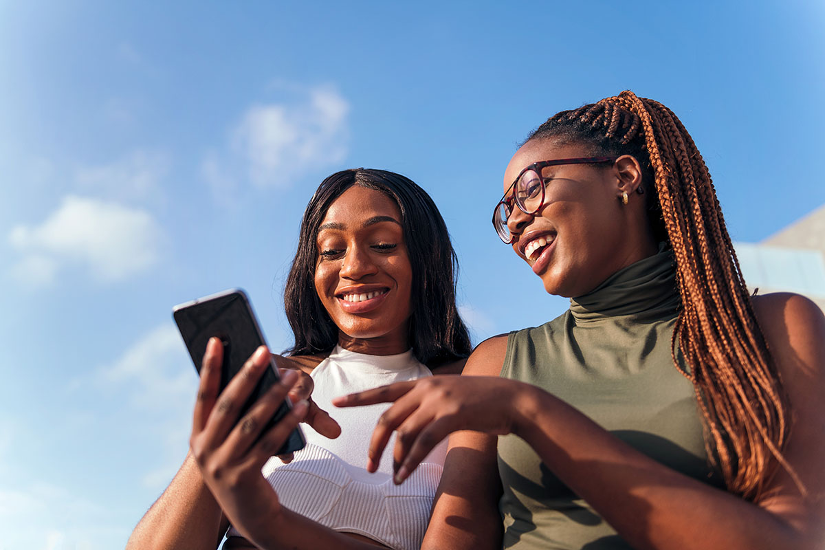 two young African women having fun together while looking at a smartphone